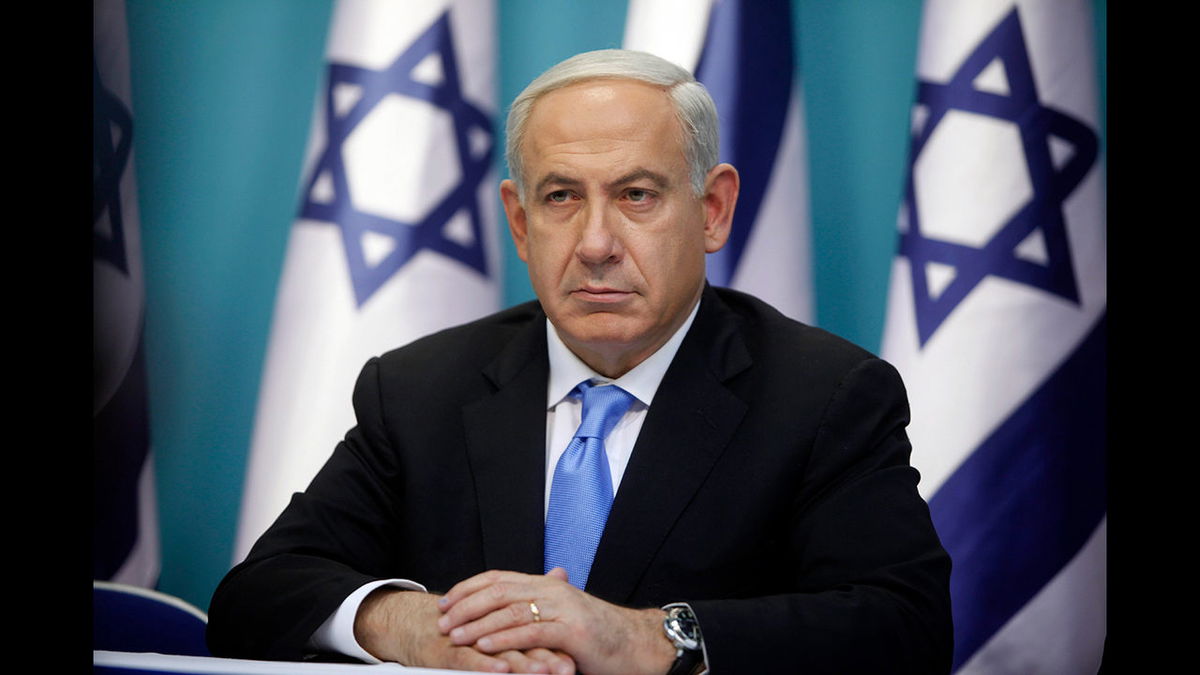 Former Prime Minister Benjamin Netanyahu sits in front of Israeli flags.