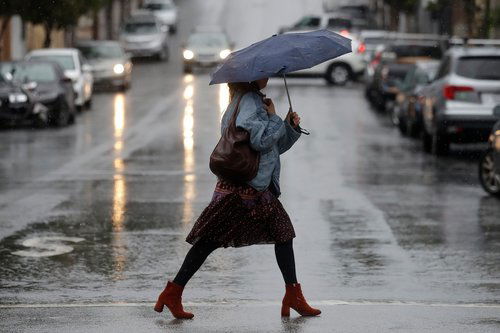 A woman crosses the street with an umbrella during a downpour on the day before Thanksgiving in San Francisco.