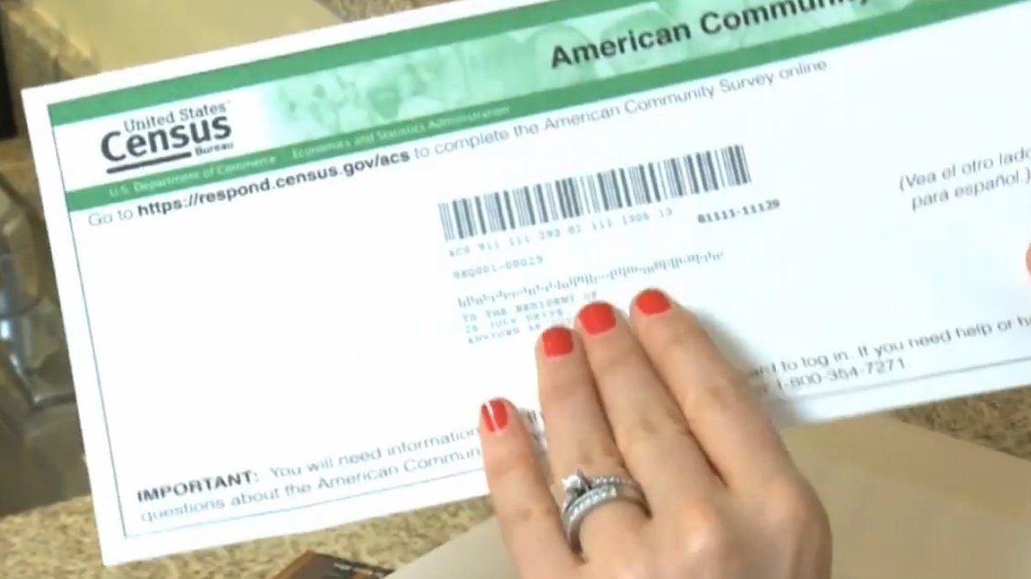 A woman holds an envelope containing a Census 2020 form.