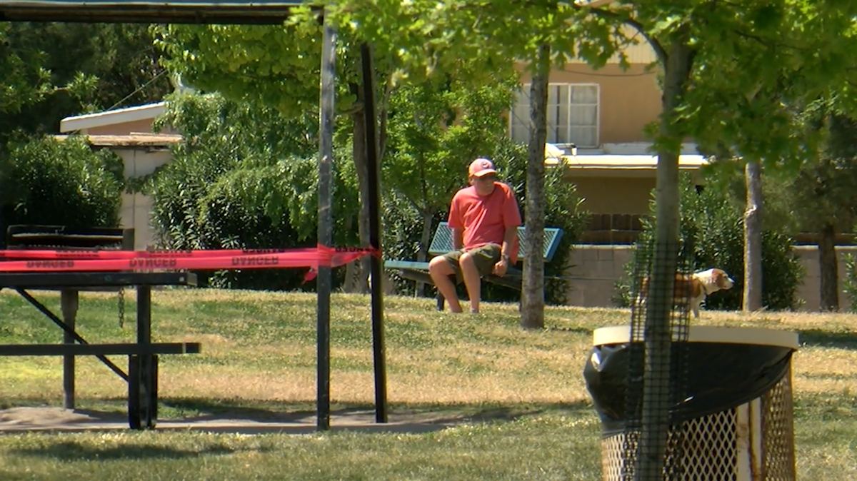 A man sits at a bench that has not yet been taped off at Young Park in Las Cruces.