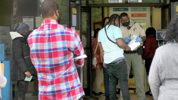 An officer wears a mask as he assists people in an unemployment line in Arkansas.