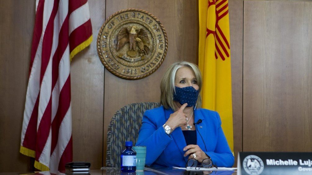 New Mexico Gov. Michelle Lujan Grisham points to her face mask as she discusses people wearing them. 