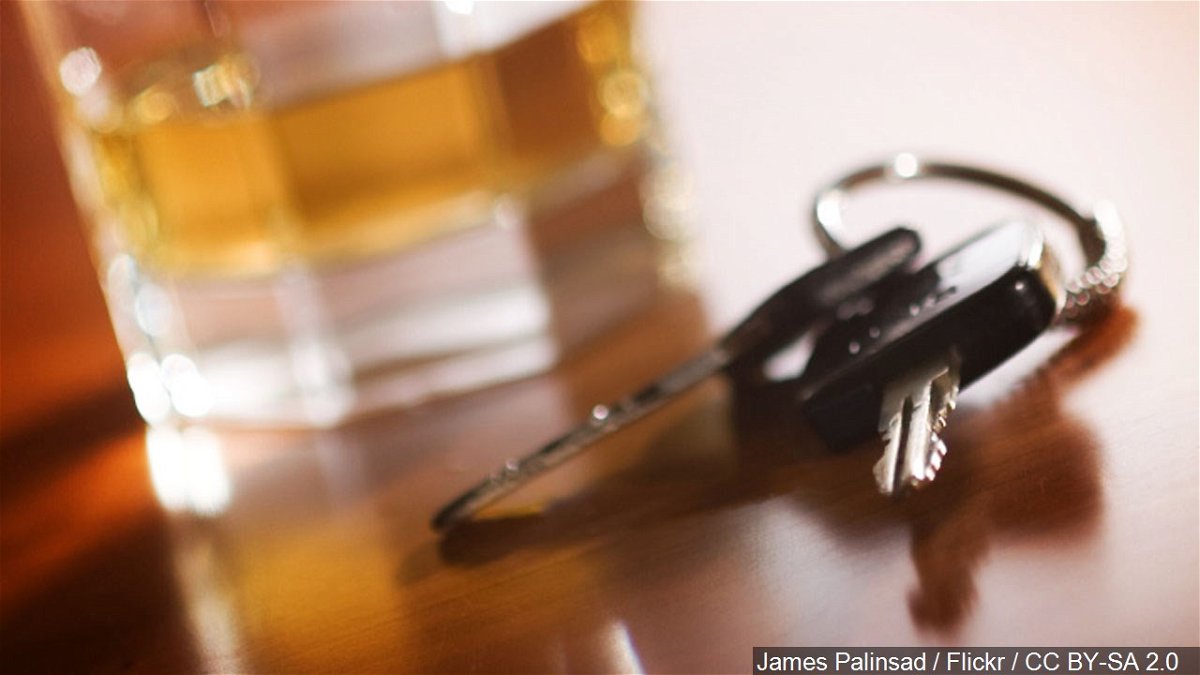 A glass of alcohol and car keys sit on a table together.