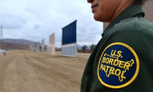 A Border Patrol agent walks near border wall examples.