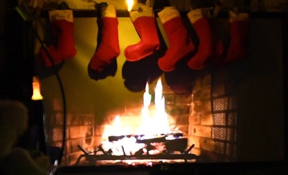 Stockings hanging above a fireplace as a yule log burns.