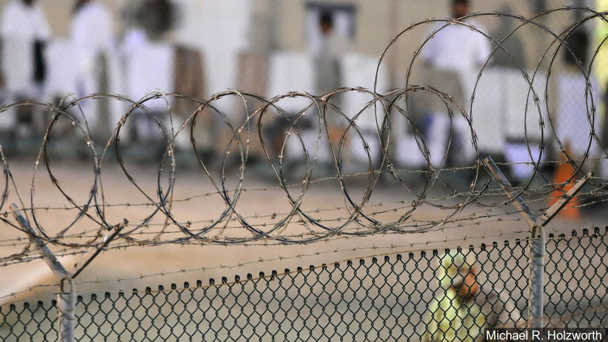 Detainees are guarded behind barb wire fence at Guantanamo Bay.