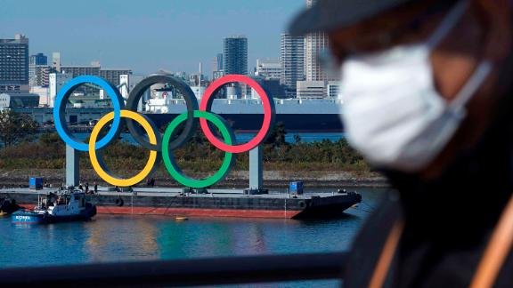 A man wearing a mask is seen walking near by an display of the Olympic rings along the Tokyo waterfront.