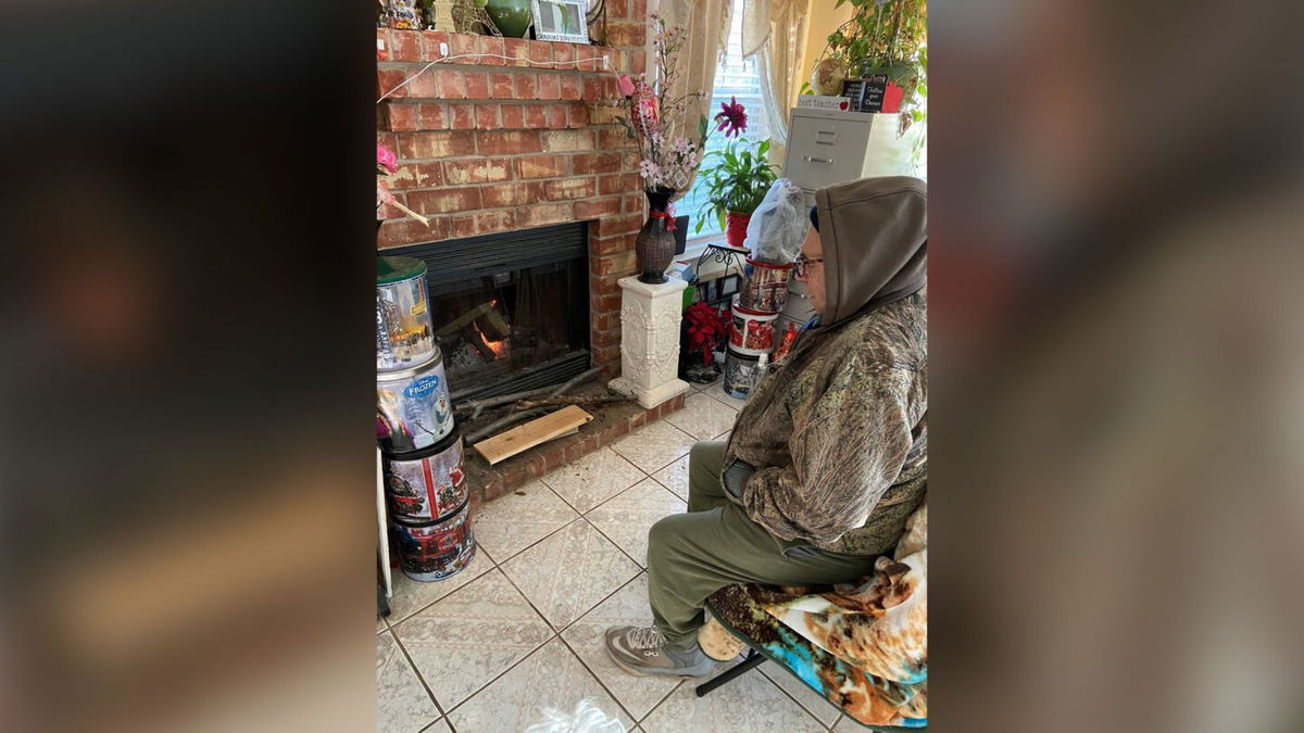 An elderly Texan trying to stay warm wearing several layers in front of his fireplace.