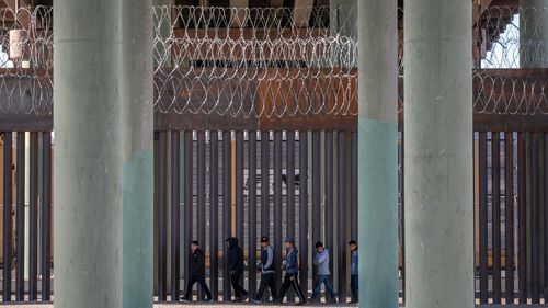 Undocumented immigrants walk along the U.S.-Mexico border wall after they ran across the shallow Rio Grande into El Paso.