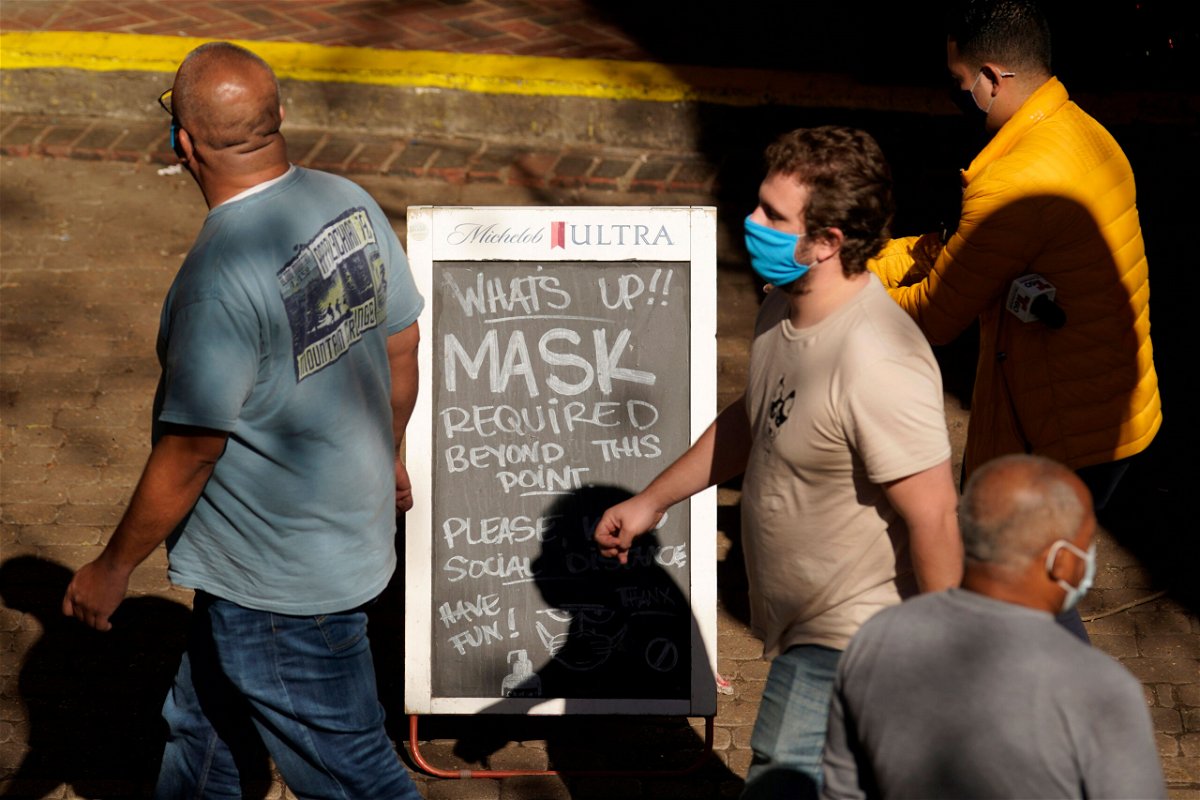 Visitors wearing face masks walk past a sign requiring masks at a restaurant along the River Walk in San Antonio, Texas.