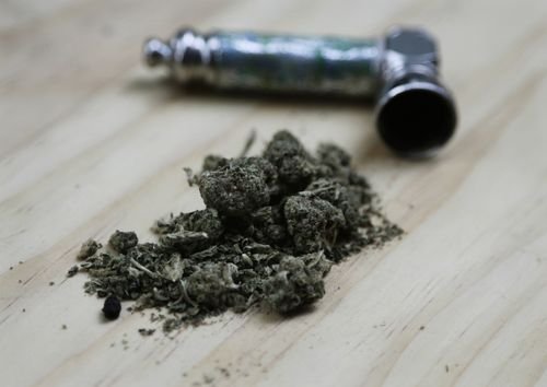 Marijuana sits on a counter-top next to a pipe used for smoking it.