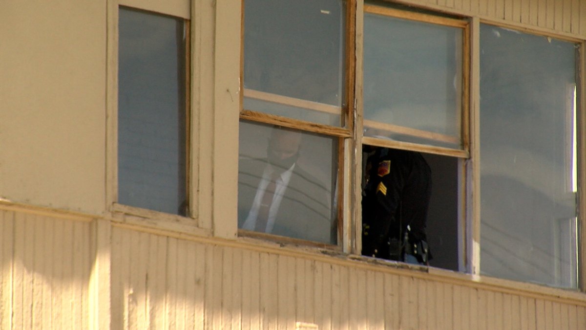 A detective and an officer can be seen through the window of an apartment where a stabbing occurred.