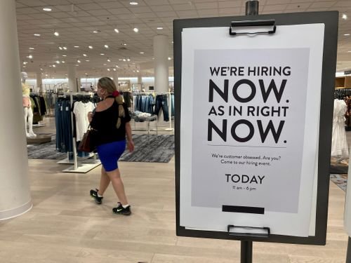 A now hiring sign is posted at the entrance to a store.