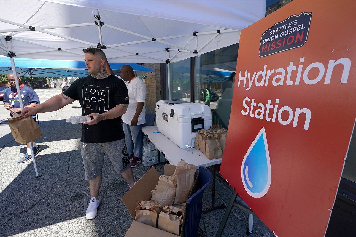 <i>Ted S. Warren/AP</i><br/>Carlos Ramos hands out bottles of water and sack luncheson Monday at a hydration station in front of the Union Gospel Mission in Seattle.