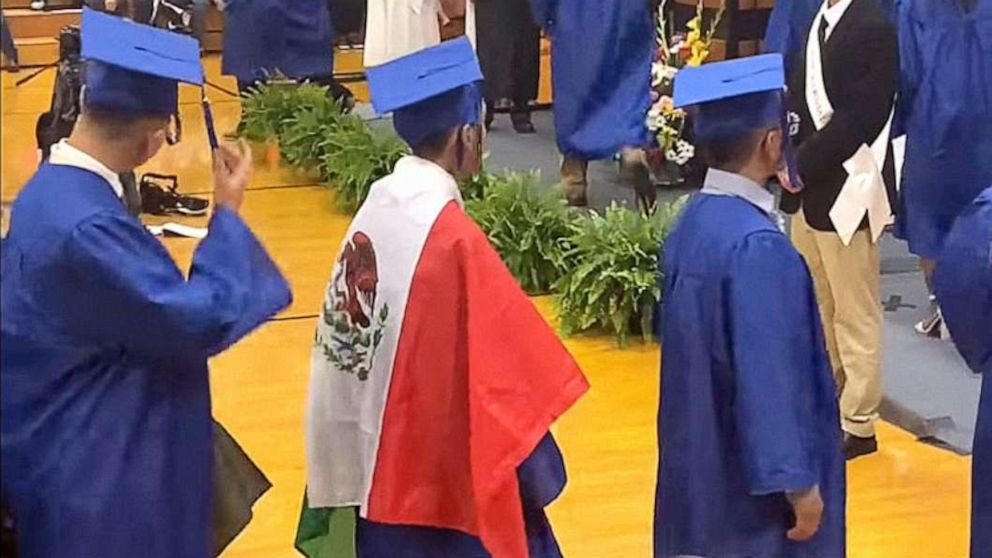 A student wears a Mexican flag over his graduation gown at his graduation ceremony.
