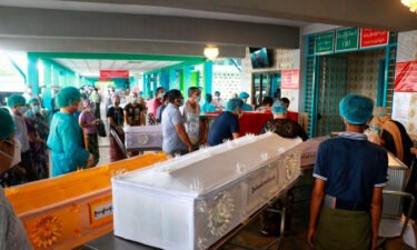 People wearing face masks wait while caskets with bodies are queued outside a crematorium at the Yay Way cemetery in Yangon