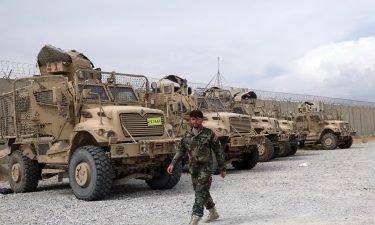 An Afghan army soldier walks past Mine Resistant Ambush Protected vehicles that were left after the American military left Bagram air base