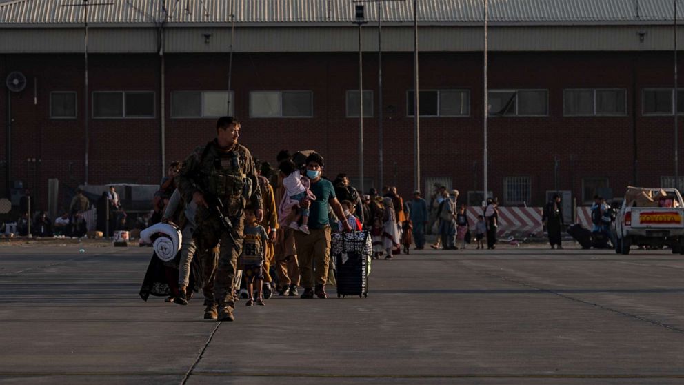 A U.S. Air Force Airman guides evacuees toward a U.S. Air Force C-17 plane during evacuations from Hamid Karzai International Airport in Afghanistan.