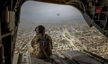 An American soldier on a CH-47 Chinook helicopter flies over Kabul