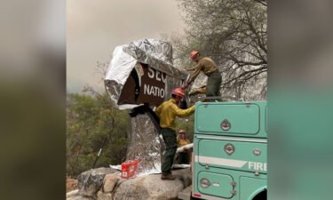 Firefighters assigned to the KNP Complex Fire prepare the historic Sequoia entrance sign for the possibility of fire in the area by wrapping it with aluminum-based burn-resistant material.