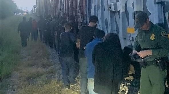 A border agent is seen along with 18 migrants found crammed into a freight rail car.
