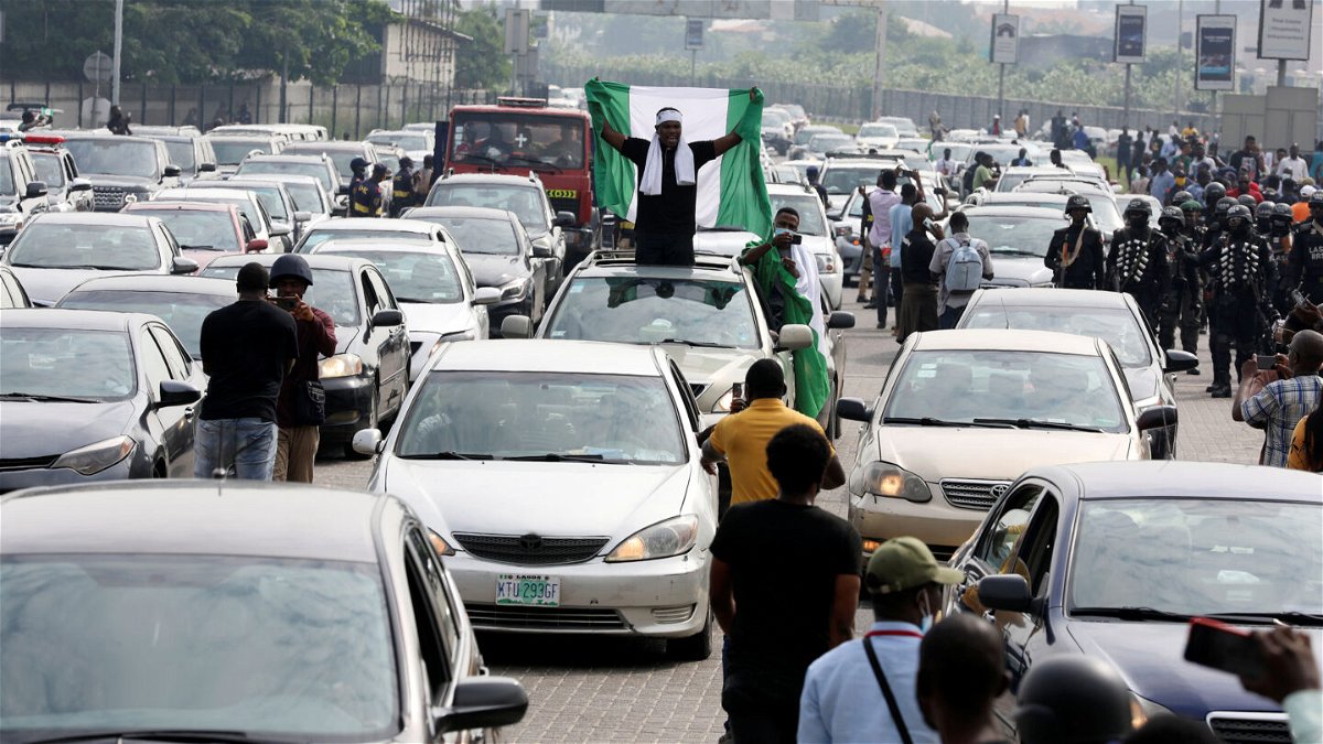 <i>Temilade Adelaja/Reuters</i><br/>A demonstrator raises a Nigerian flag from a car during a motorcade to mark the one-year anniversary of the #EndSARS protest at the Lekki toll gate in Lagos