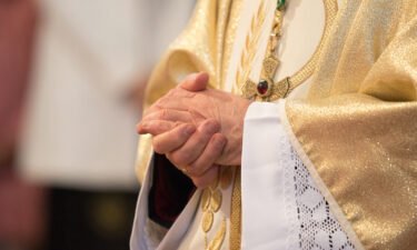 A Catholic priest holds praying hands.