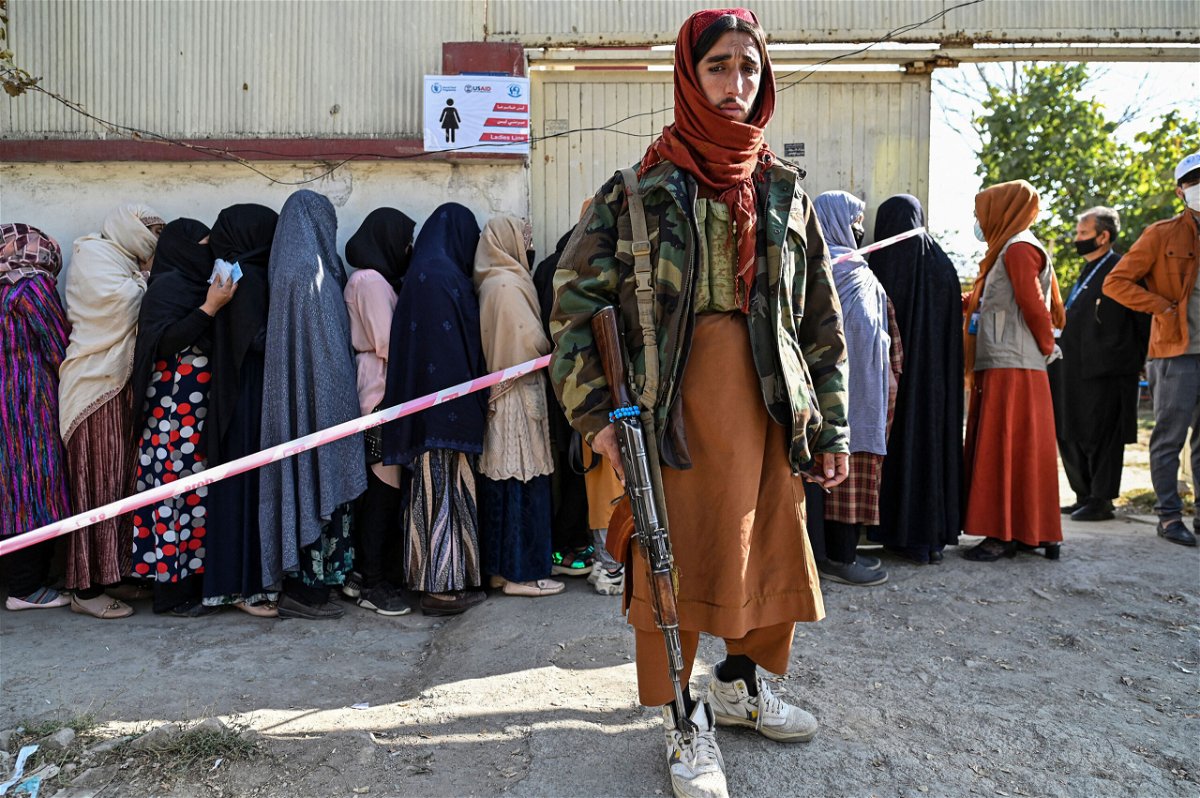 <i>HECTOR RETAMAL/AFP via Getty Images</i><br/>A Taliban fighter stands guard as women wait in line for food from the World Food Programme in Kabul on November 6.