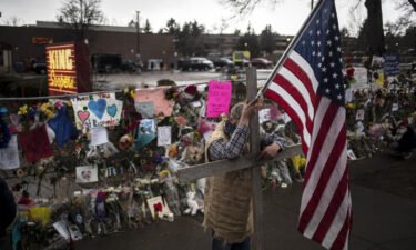 A mourner leans on a cross while holding a flag outside a memorial at a King Soopers Grocery store on March 26