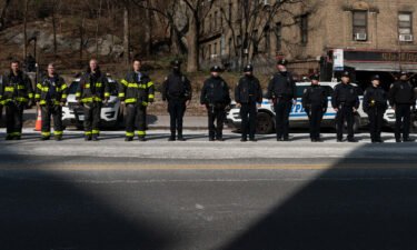 New York City police officers and firemen stand at attention as they await the remains of Police Officer Jason Rivera to be brought to the funeral home on January 23 in New York City.