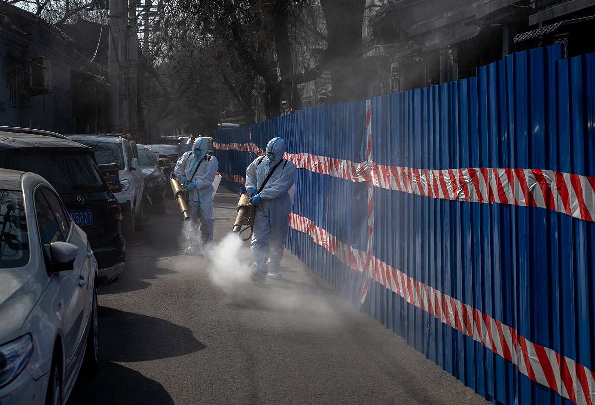 <i>Kevin Frayer/Getty Images</i><br/>Workers in protective suits disinfect an area outside a barricaded community that was locked down for health monitoring after recent cases of Covid-19 were found in the area on March 28