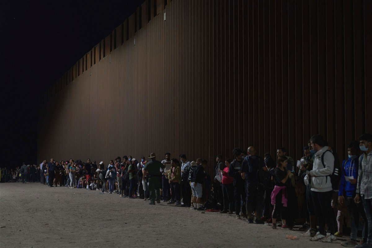 TOPSHOT - Migrants line up as they wait to be processed by US Border Patrol after illegally crossing the US-Mexico border in Yuma, Arizona in the early morning of July 11, 2022.
