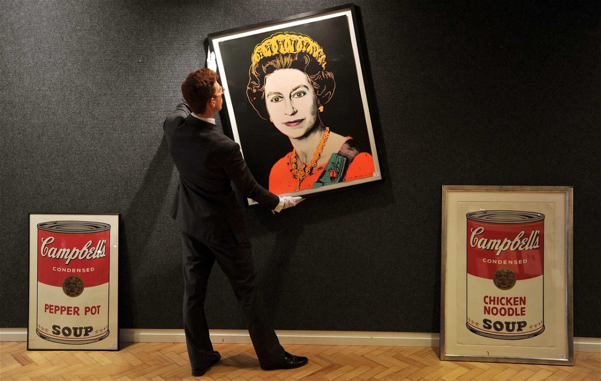 <i>John Stillwell/PA Images via Getty Images</i><br/>An employee of Bonhams Auctioneers adjusts a print by Andy Warhol of Queen Elizabeth II.