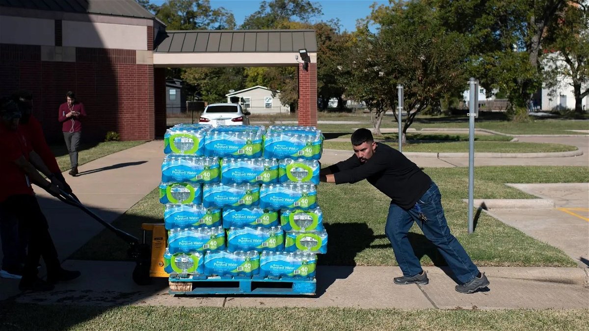 Isaiah Chirip helps push a pallet of bottled water during a water distribution and free flu vaccination event at the Holman Street Baptist Church in Houston on Nov. 28, 2022.