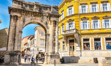 An ancient Roman arch stands in a sunny square in Pula