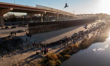 Migrants queue near the border wall to request asylum in El Paso