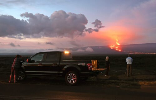 People stand on the side of the road to photograph the eruption of the Mauna Loa volcano on December 04
