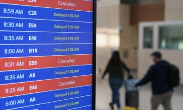 Travelers walk as a video board shows flight delays and cancellations at Ronald Reagan Washington National Airport in Arlington