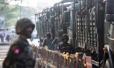 Soldiers stand next to military vehicles as people gather to protest against the military coup