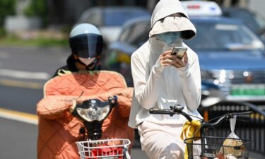 A woman wearing sun protective clothing commutes on a bicycle amid hot weather in Shanghai on Monday.