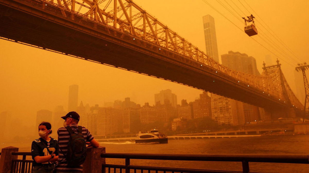 <i>Shannon Stapleton/Reuters</i><br/>People wear protective masks as the Roosevelt Island Tram crosses the East River while haze and smoke from the Canadian wildfires shroud the Manhattan skyline in the Queens Borough New York City