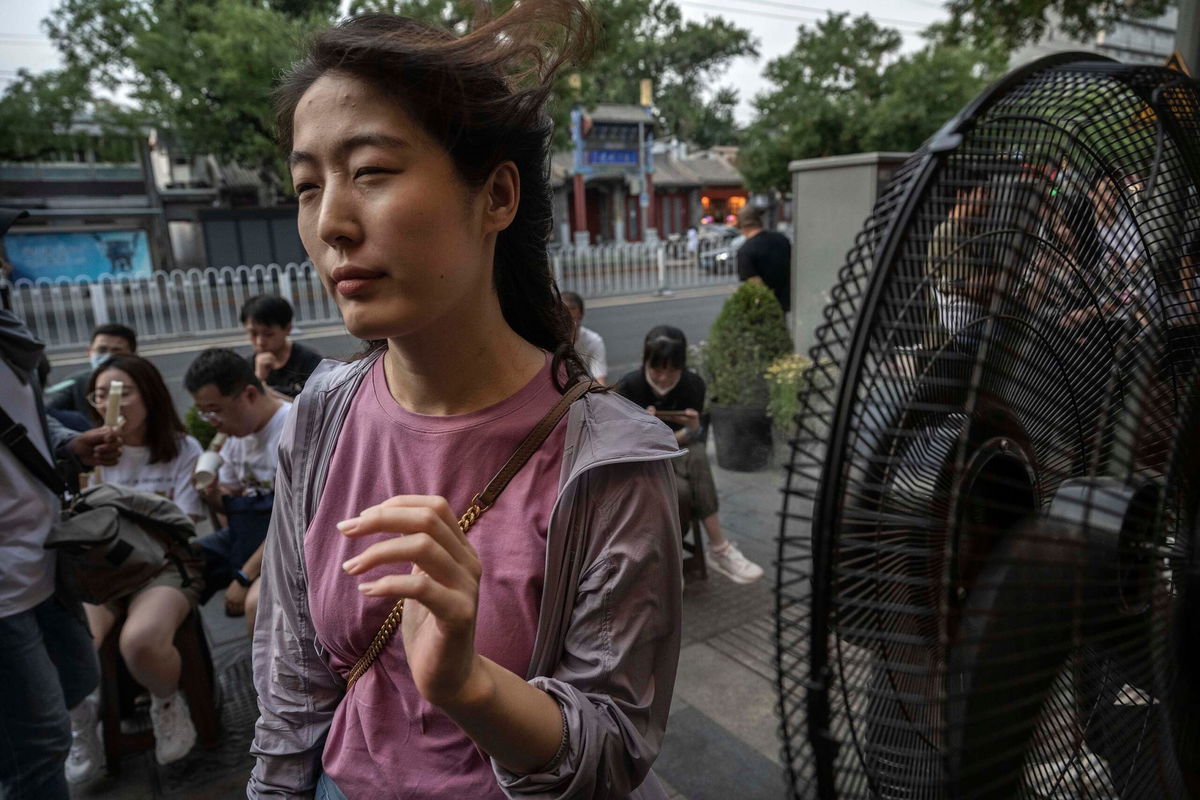 <i>Kevin Frayer/Getty Images</i><br/>A woman cools herself on a misting fan as she waits for a table outside a popular local restaurant during a heatwave on June 23