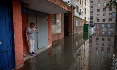 Olena stands next to the entrance to her house on a flooded street