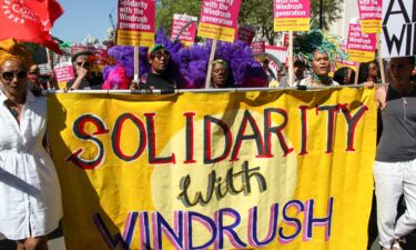 Protesters hold a sign reading "Solidarity with Windrush."