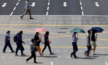 People in Singapore shield themselves with umbrellas from the glaring sun as they cross a street.