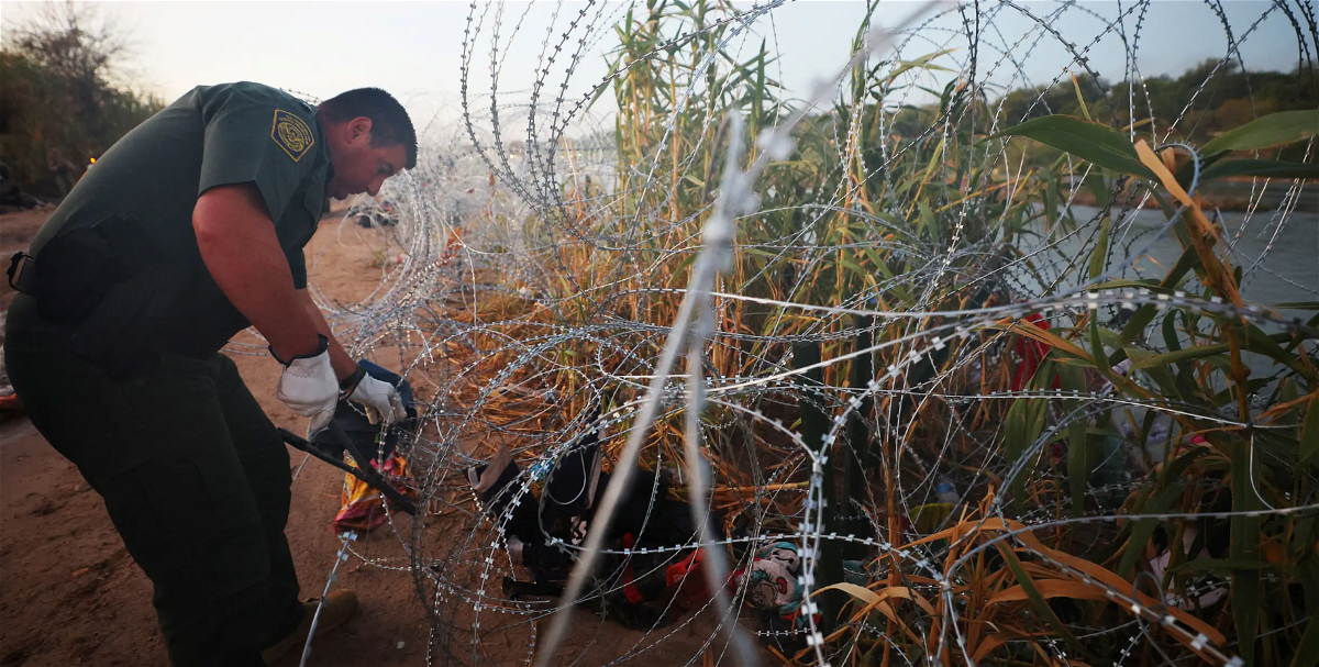 A U.S. Border Patrol agent cuts through concertina wire to let a group of asylum seekers through after they crossed the Rio Grande at Eagle Pass. Texas, which deployed the wire at the border, is suing the Biden administration, claiming it illegally destroyed state property.