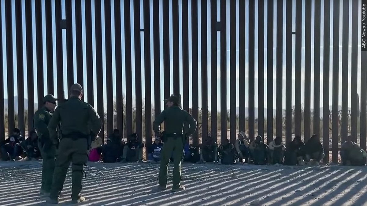 Migrants and border agents wait near a border barrier