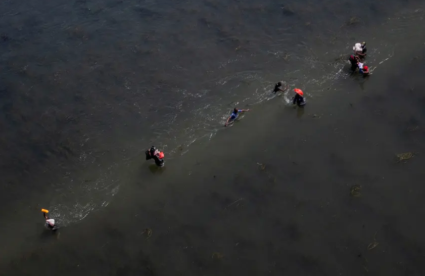 Migrants seeking refuge in the U.S. cross the Rio Grande back into Ciudad Acuña, Mexico as others return to the U.S. carrying food near Del Rio on Sept. 19, 2021. A new Texas law that makes illegal immigration a state crime is being challenged in court by the federal government.
