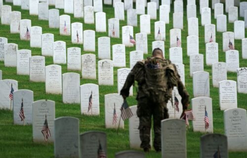 A US Army Old Guard soldier places a flag at a headstone during the annual 'Flags In' event ahead of Memorial Day at Arlington National Cemetery in Arlington