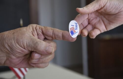 Poll worker Kenny Smith hands a sticker to a voter on Super Tuesday in Stillwater
